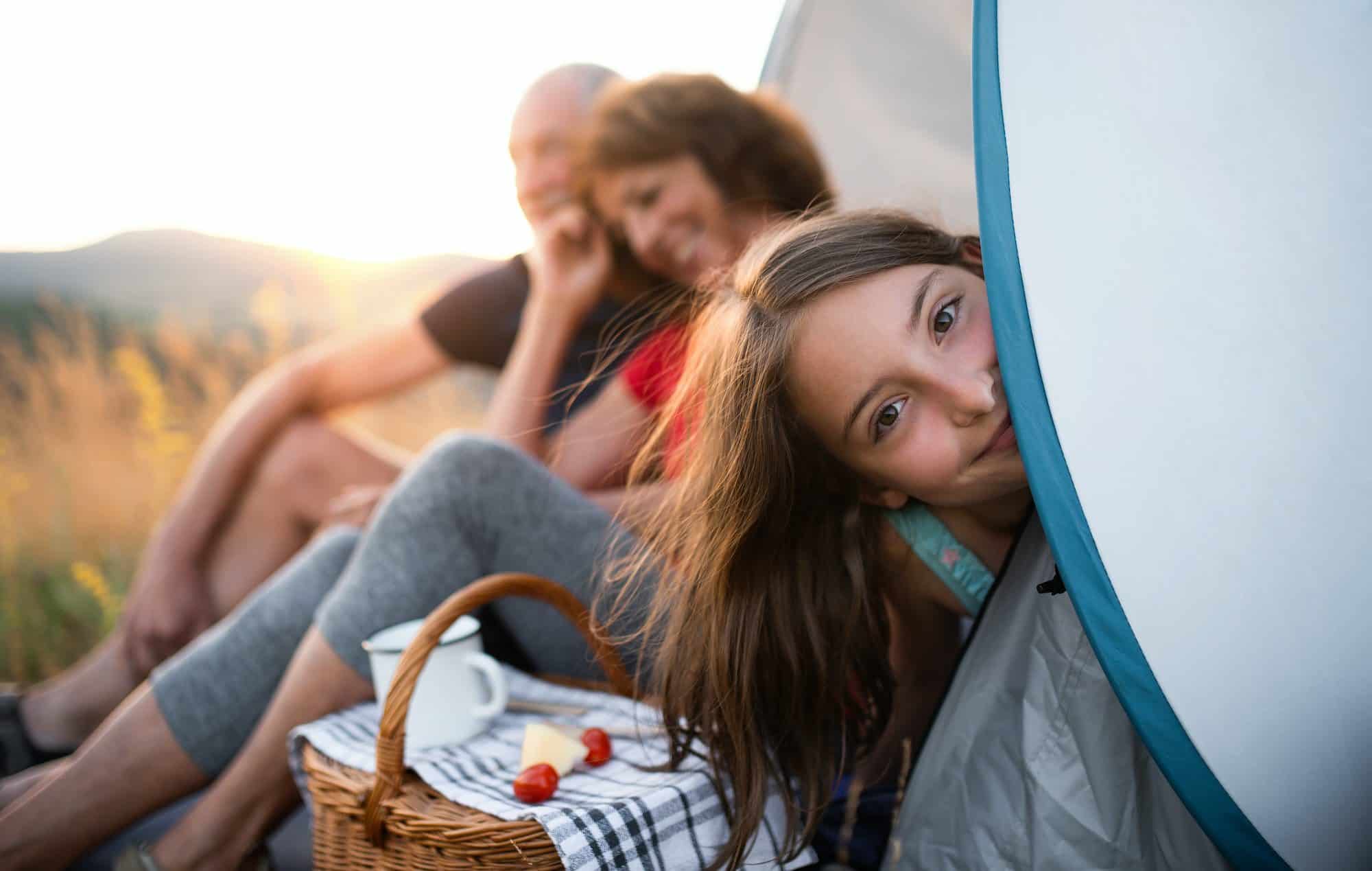Small girl with grandparents sitting in shelter tent in nature at sunset, resting