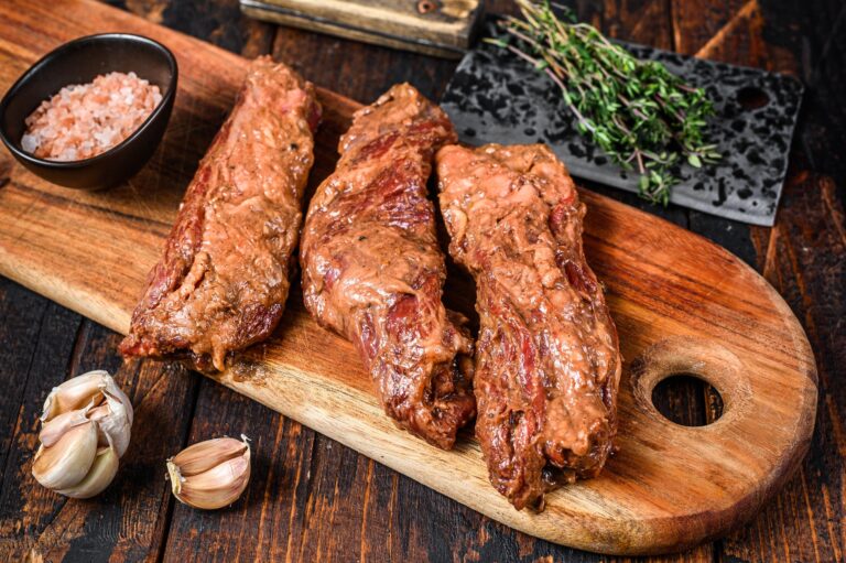 Raw Marinated skirt steaks in bbq sauce on a wooden cutting board with herbs.