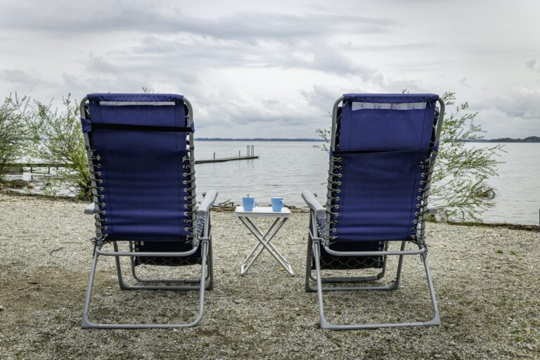 two camping chairs on a gravel beach overlooking the water and a wooden deck
